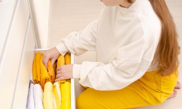 Women putting away yellow clothing in a draw