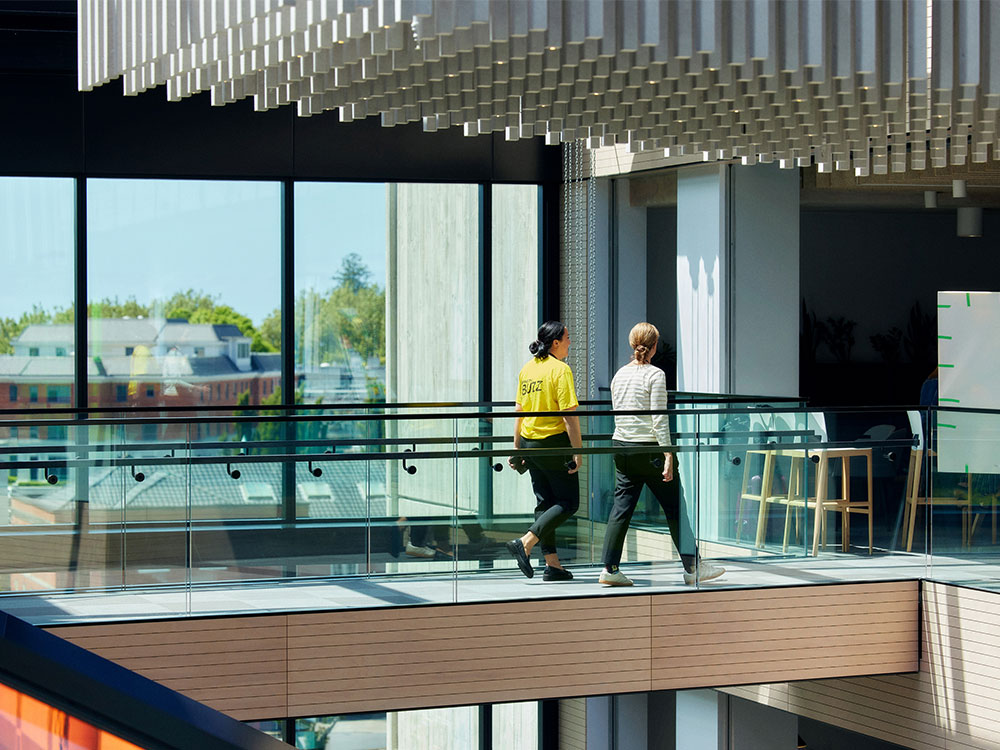 Two people walking along a walkway of in a modern building. 
