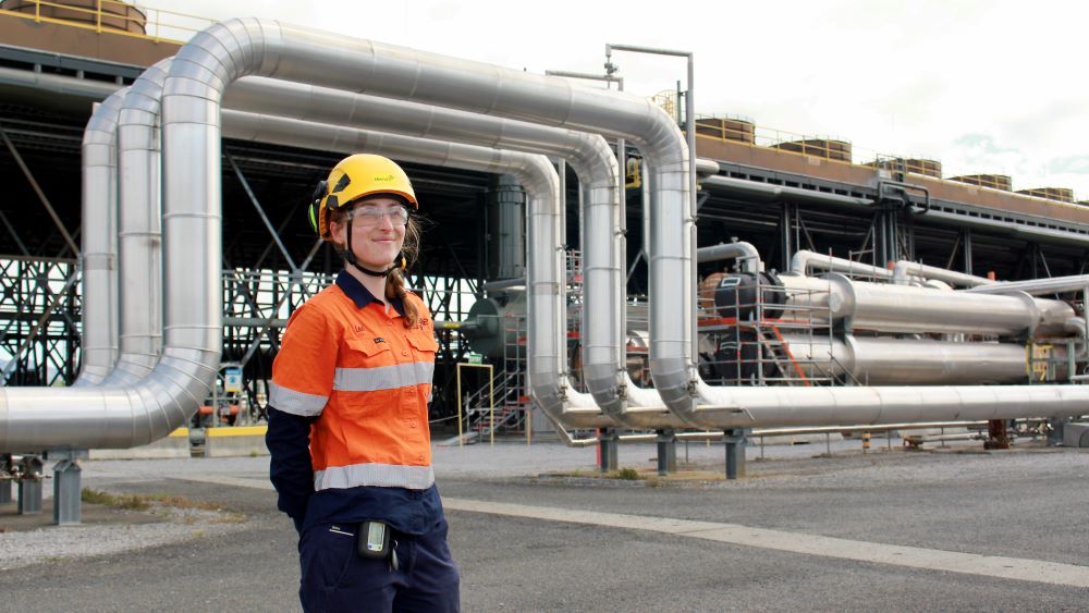 Lexi Richards at Nga Tamariki Geothermal Power Station with pipes behind her