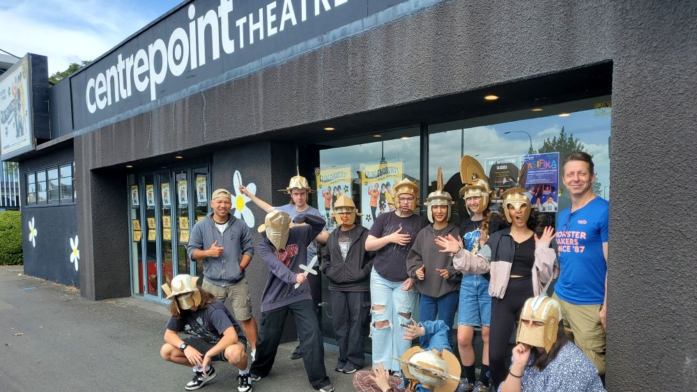 Group of young people posing wearing theatrical Roman helmets outside a theatre