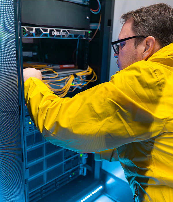 Man in yellow jacket working with data racks.